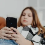 A teenage girl relaxes on a sofa at home while using her smartphone.