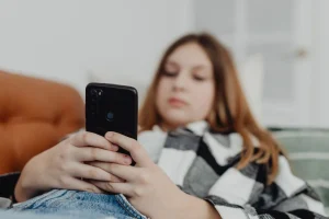 A teenage girl relaxes on a sofa at home while using her smartphone.